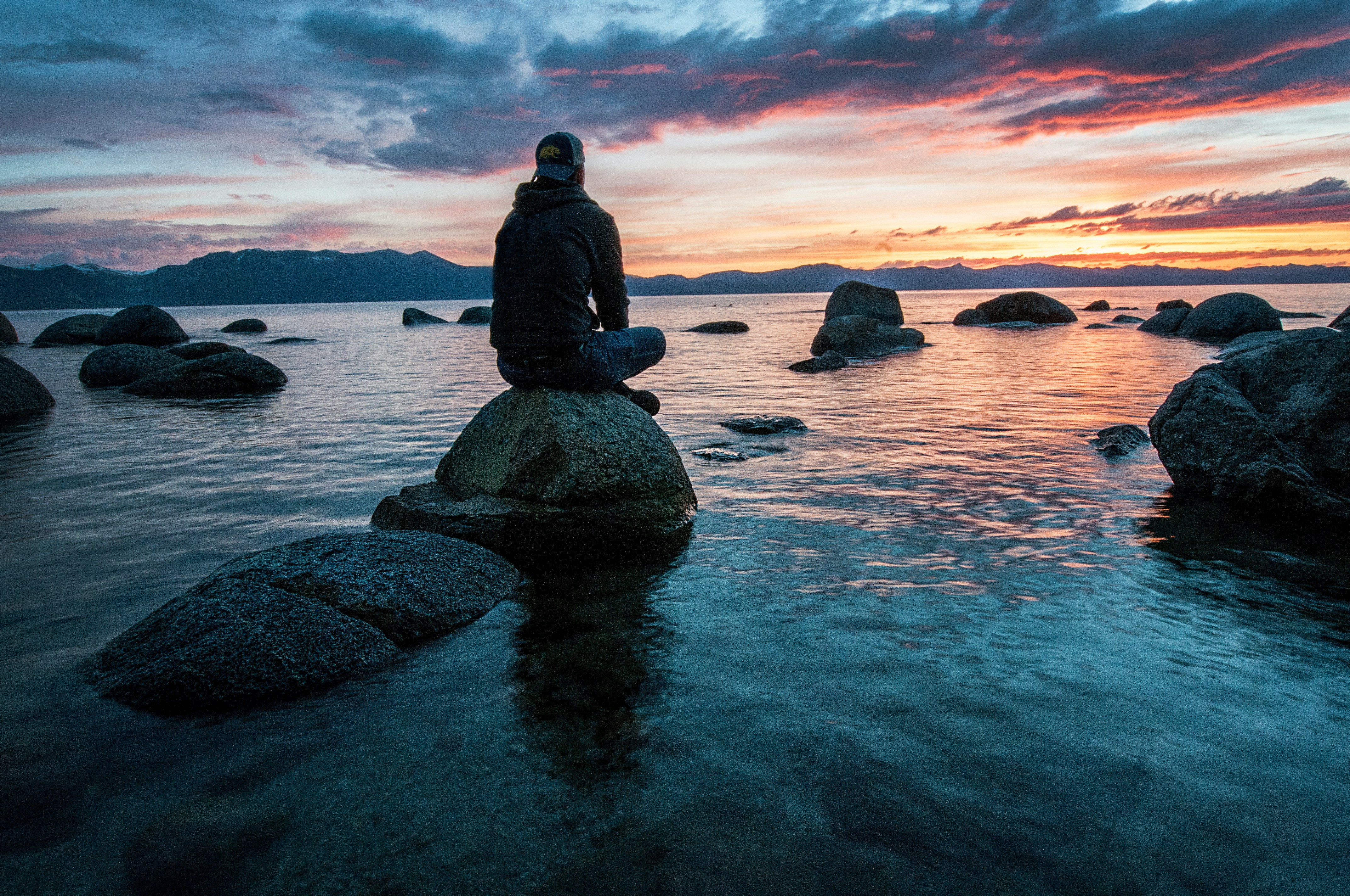 A person sitting quietly on a rock by a lake at sunset, doing nothing in particular